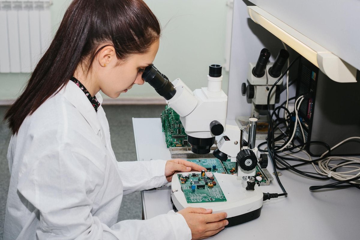 Technician inspecting an assembled circuit board under a stereo microscope